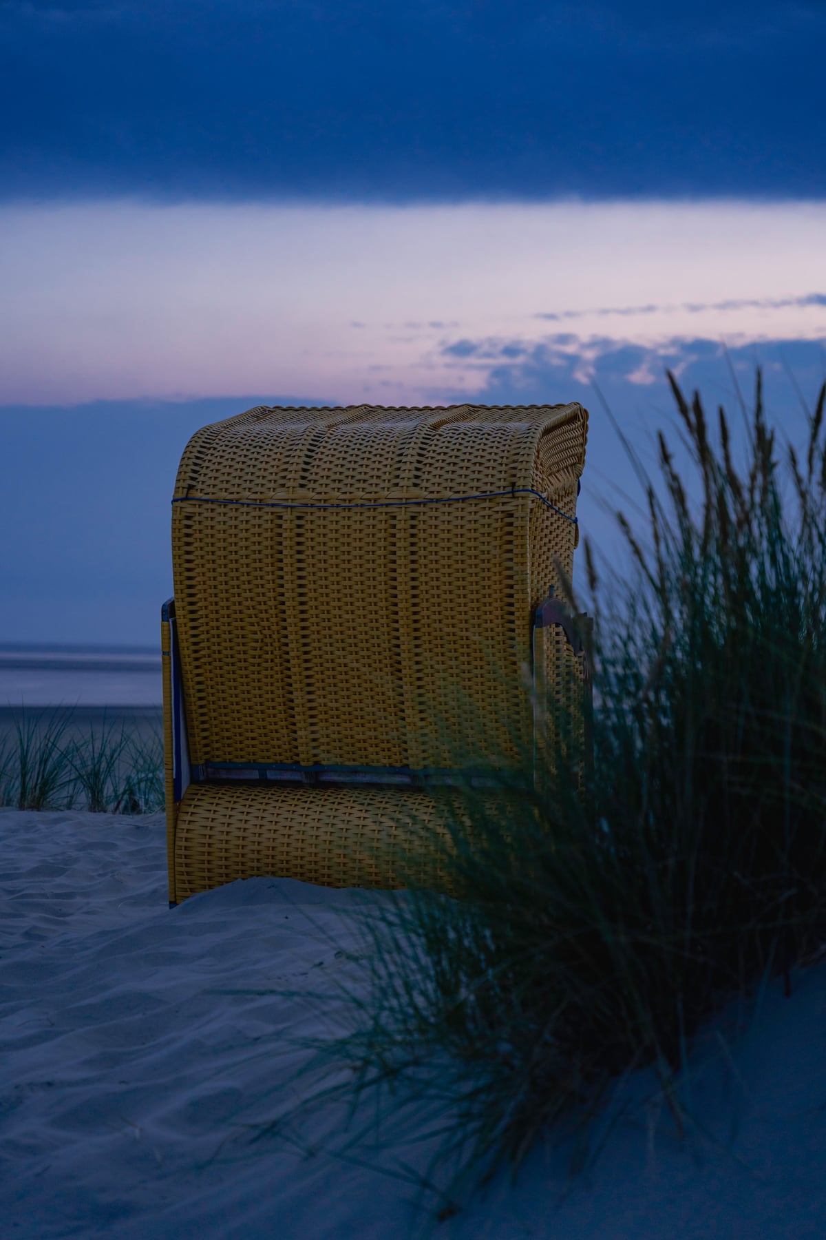 Gelber Strandkorb zwischen Dünenhalmen in der blauen Stunde auf Borkum
